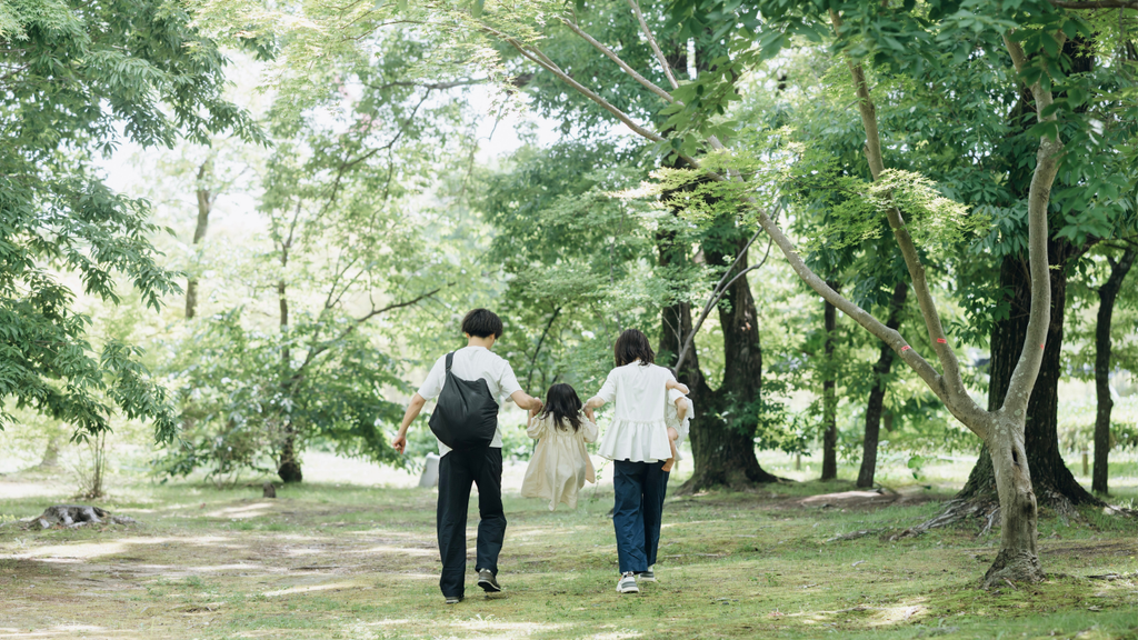 緑の公園を歩く両親と子どもの後ろ姿