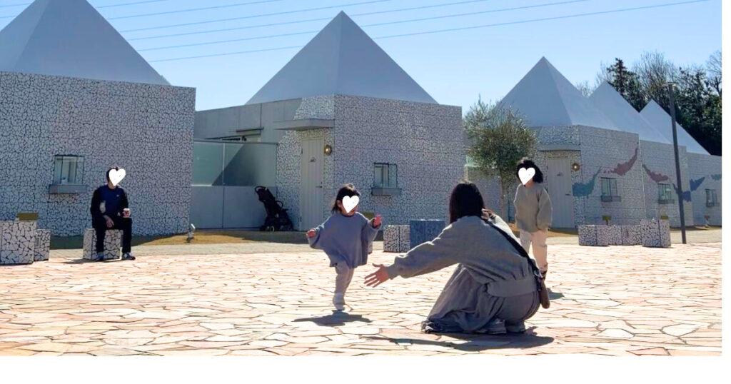 旅行先の広場で、しゃがんで待つ母親へ走っていく子どもと家族